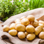 Farm fresh baby potatoes displayed on a hessian sack on a rustic wooden table at farmers market, a healthy nutritious root vegetable popular in vegetarian and vegan cuisine